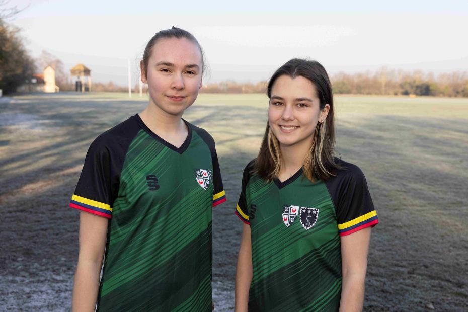 two  playersof the girton and murray edwards women's football team standing on the sports pitches
