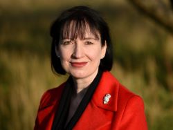 Dr Suzy Lishman stands outside, there are trees in the background