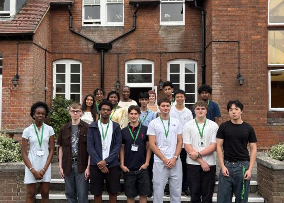 16 students dressed smartly outside a red-brick building at Girton College, University of Cambridge