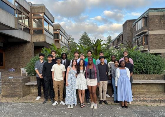 A group of students dressed smartly in front of green plants at Churchill College, Unviersity of Cambridge