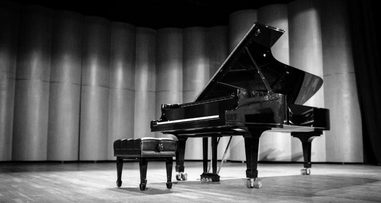 Black and white photograph of piano and stool on stage