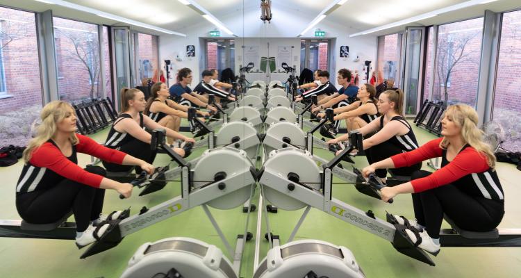Rowers lined up on erg machines with their reflections showing in the mirror