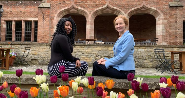 Sigourney Bonner (left) and Dr Elisabeth Kendall (right) sitting on a wall looking back in the Fellows Gardens with a row of orange, purple, and cream tulips in the foreground