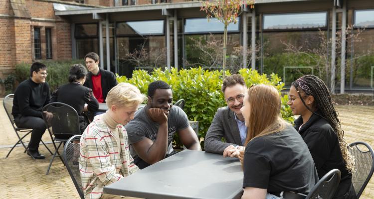 Girton students sitting around at tables in conversation in Ash Court