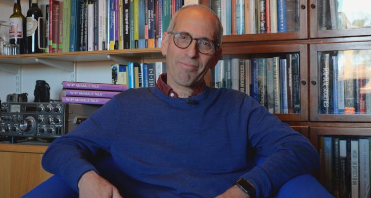 Dr Arik Kershenbaum sitting in his Girton College Office with shelves full of books behind